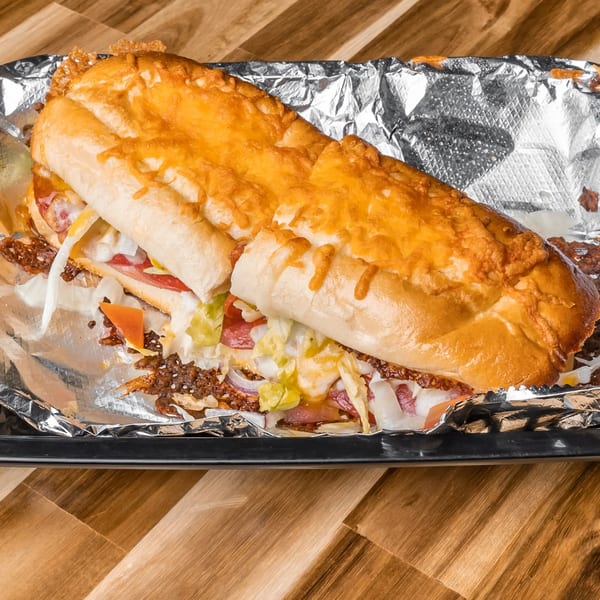 A large, cheesy Slammers sub sandwich with meat, lettuce, and tomatoes, served in foil.