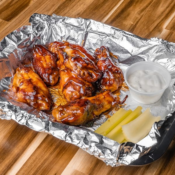 Slammers' BBQ chicken wings with ranch dressing and celery sticks in a foil-lined container.
